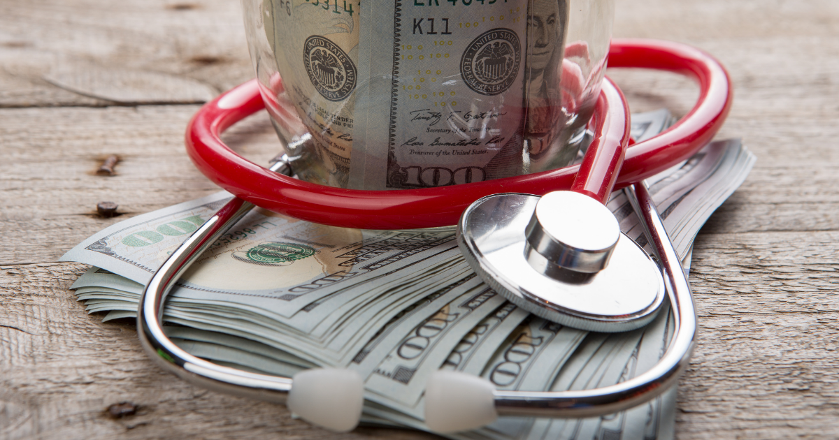A jar of money wrapped in a stethoscope sits on top of a stack of cash.