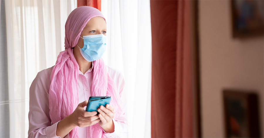 A woman going through chemo is wearing a mask and holding a wallet in her hand, representing how COVID-19 policy helps the cancer community.