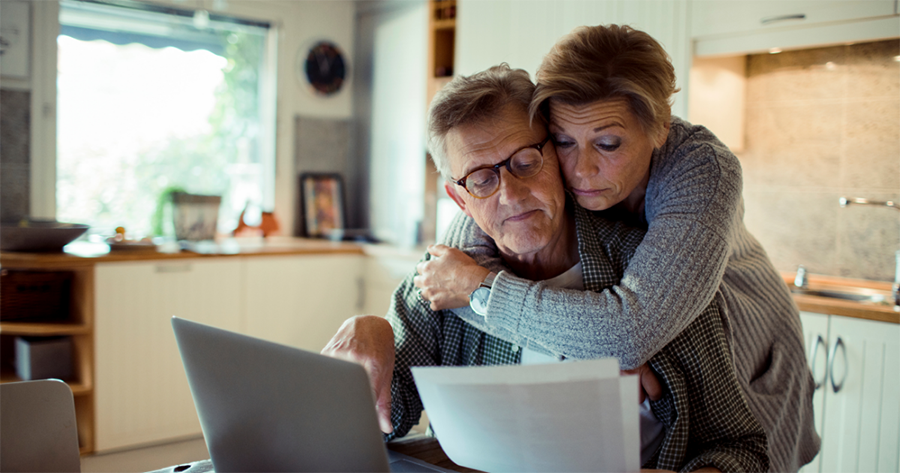 A man and woman look sadly at a piece of paper, theoretically a bill from cancer treatment that is past due and could impact their credit score.