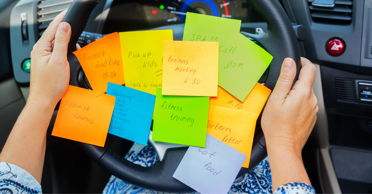 A person has their hands on their car steering wheel. It's covered in sticky notes with to-dos, representing caregiver productivity.