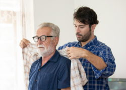 A man, who could benefit from paid leave for caregivers, helps his elderly father get dressed.