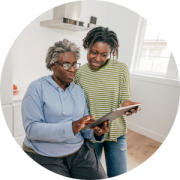 An older person and a younger person are together in a room looking at a tablet, representing the cancer caregivers rights and resources webinar.