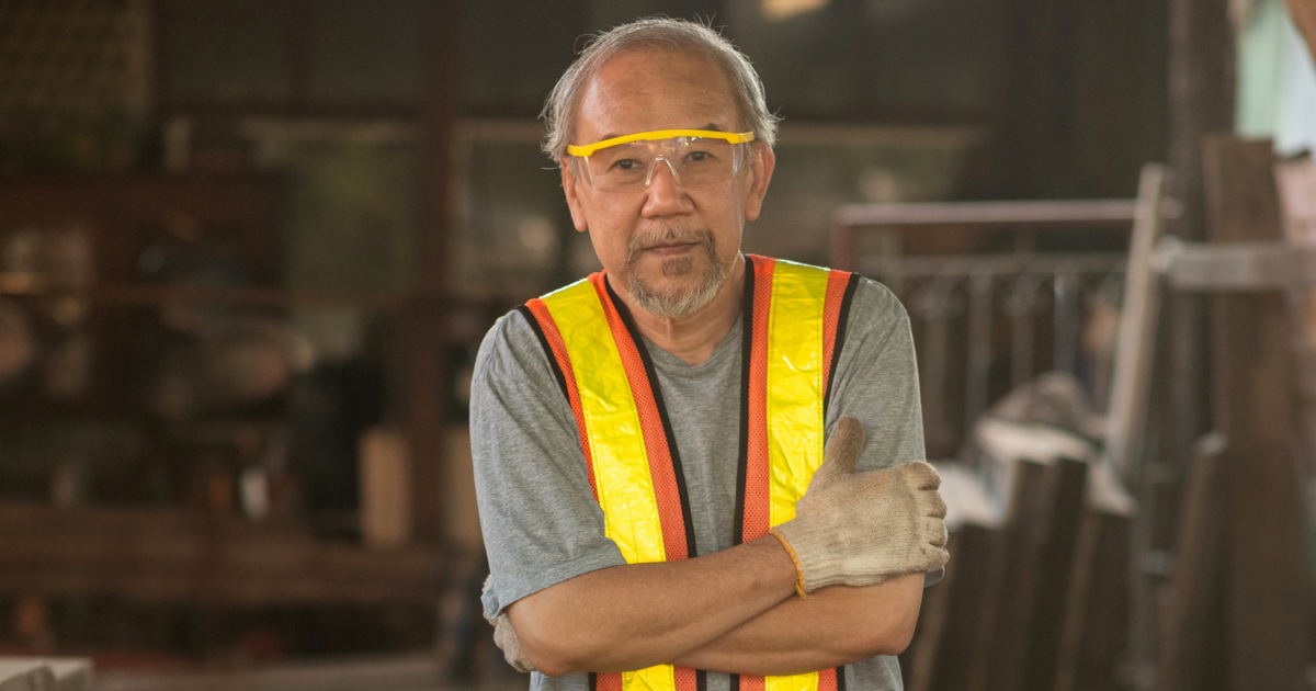 A male construction worker dressed in a bright work vest and wearing safety goggles.
