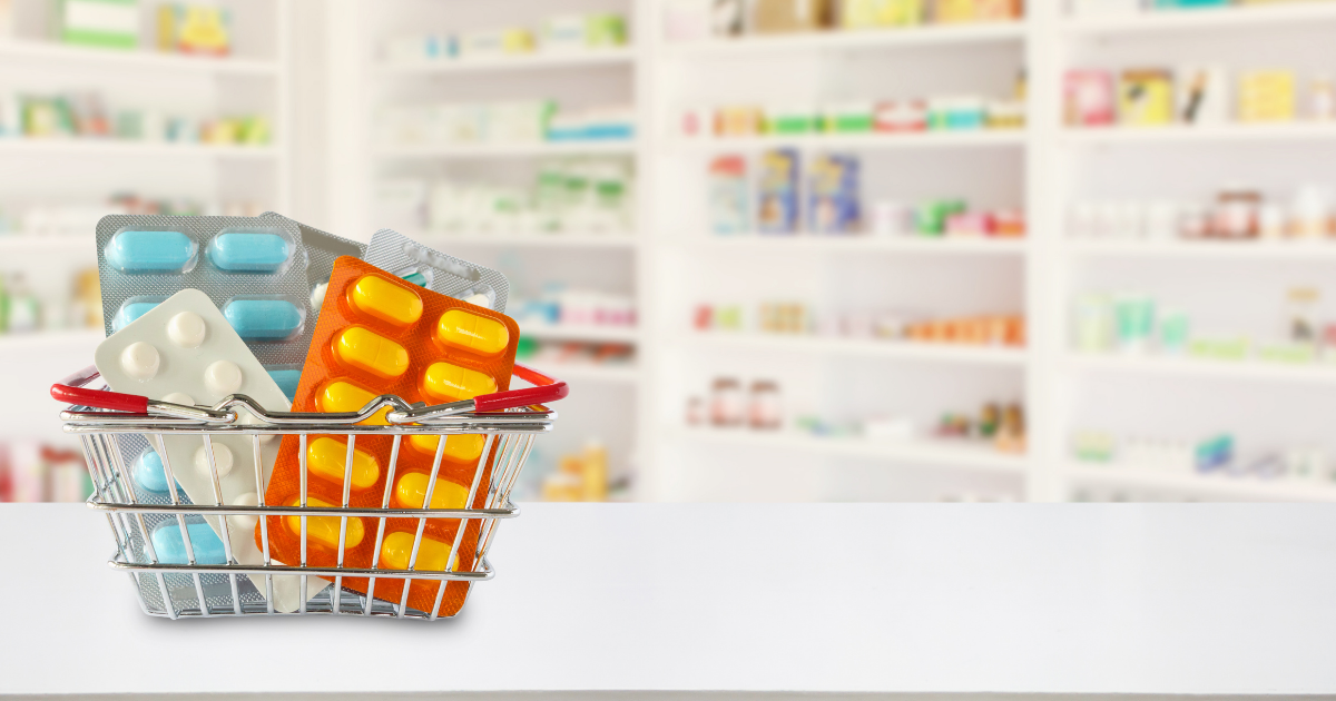 A Pharmacy Benefit Manager (PBM) is a company that selects, purchases, and distributes drugs for a health insurance company. A shopping basket of pills sits on top of a counter with prescriptions in the background.