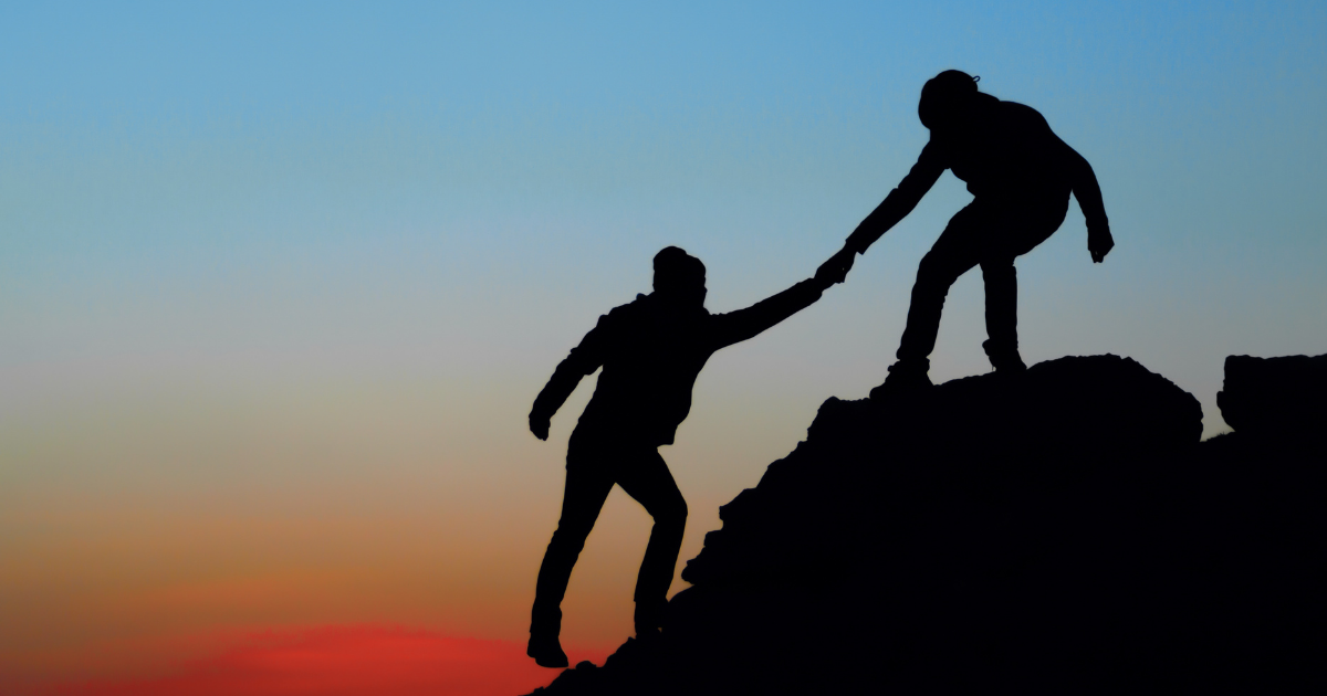 A person helps another person up a mountain.