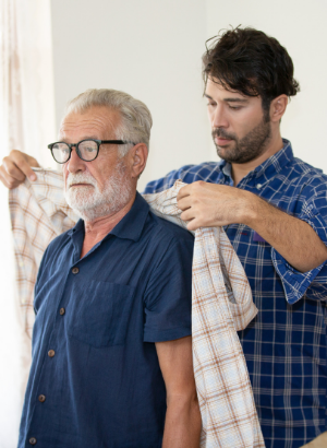A young man helps an older man put on a jacket.