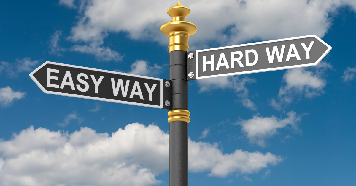 A street sign sits against a blue sky. One sign says "easy way" and points left, and the other "hard way" and points right.