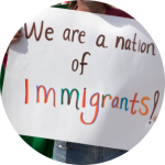 A person is holding up a sign that says "We are a nation of Immigrants" in colorful ink.