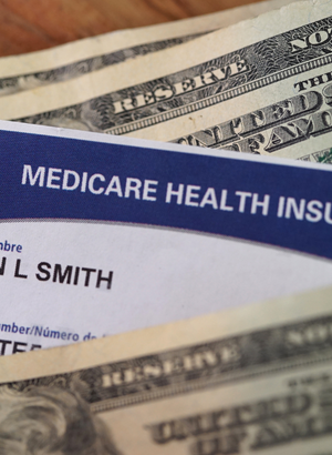 A Medicare health insurance card sticks in a stack of $20 bills