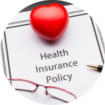 A health insurance policy sits on a desk with a foam heart, pair of glasses, and a pen on top of it.