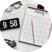 A Januarycalendar, a phone with a clock, a water bottle, and a pair of glasses all sit on a desk.