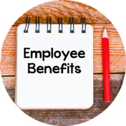 A note pad sits on a desk with the words "employee benefits" written on it. A red pencil is sitting on the desk next to it.