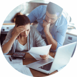 A man and a woman are at the kitchen table looking worried about finances.