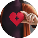 A woman holds up a paper cut out of red heart with a medical cross in the middle of it.