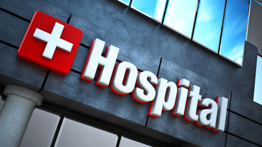 The front of a hospital with the white cross on a red background.