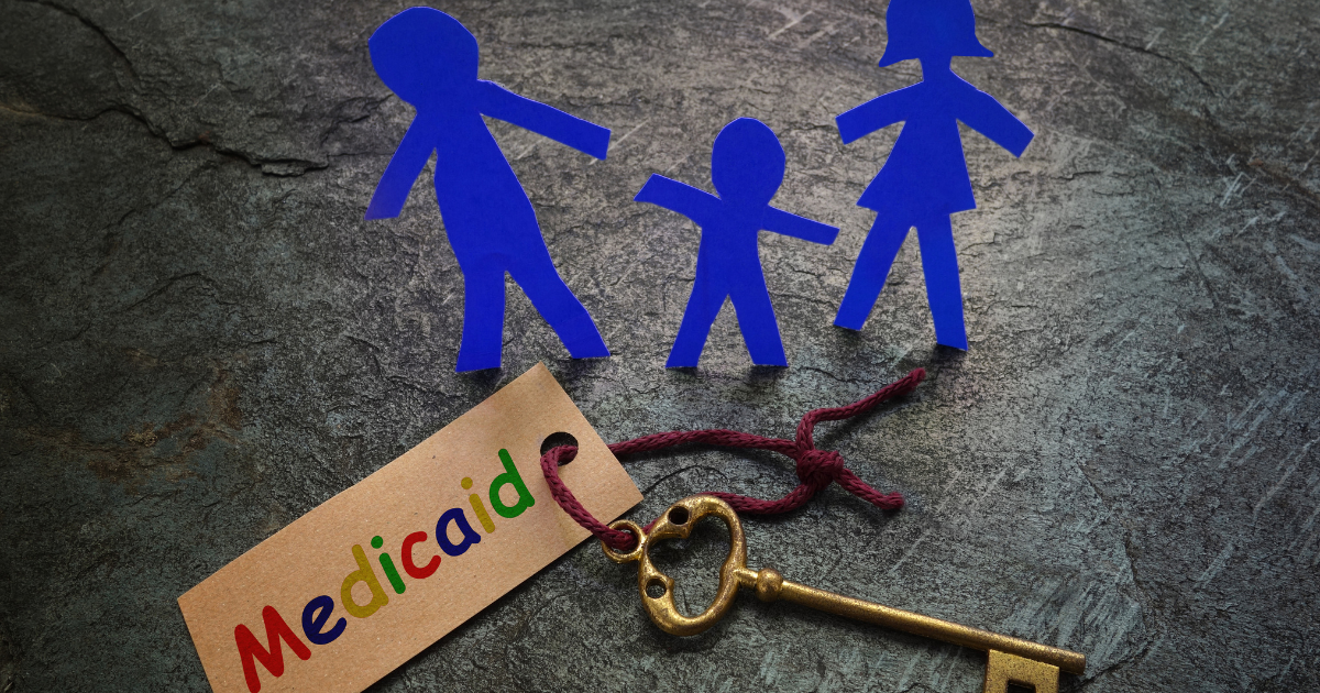 A blue paper family stands up next to a key with a tag on it that says "Medicaid" in a rainbow of colors.
