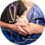 A nurse holds the hand of an elderly person in hospice care.
