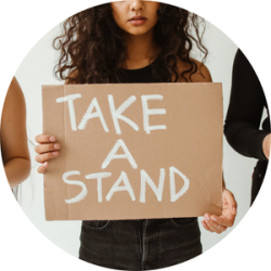 A woman is holding a cardboard sign that says "take a stand"