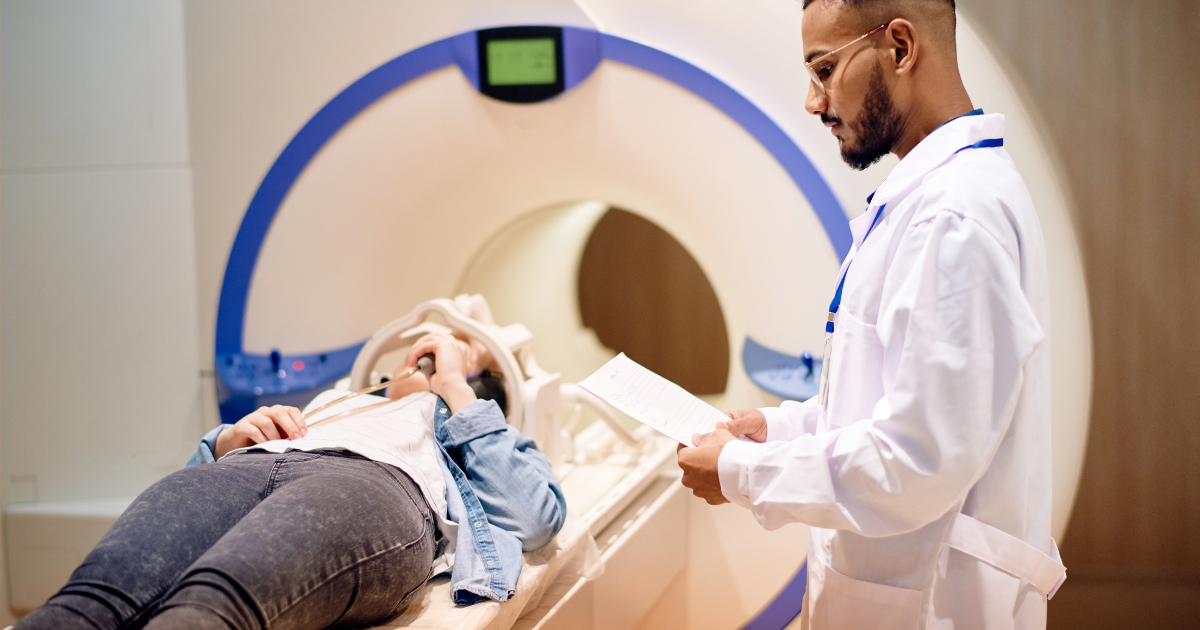 A doctor takes notes as a patient moves into the MRI machine.