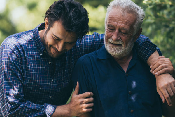 A man with his arm around his father and smiling with the text 