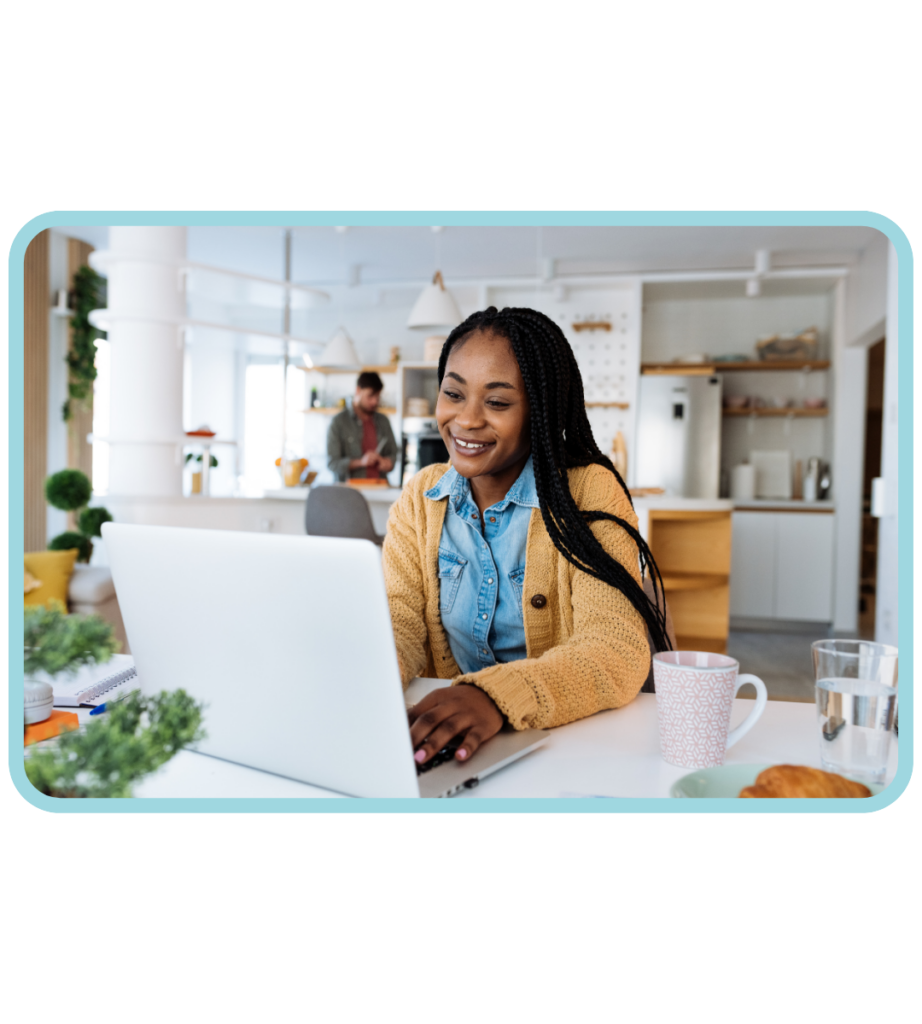 A young adult at dining table on laptop smiling while looking over health insurance resources