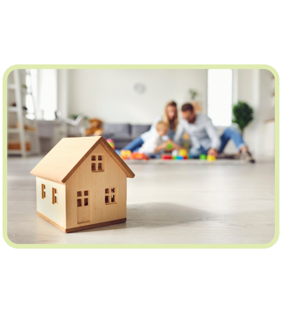 Toy wooden house with mother and father in background playing with baby